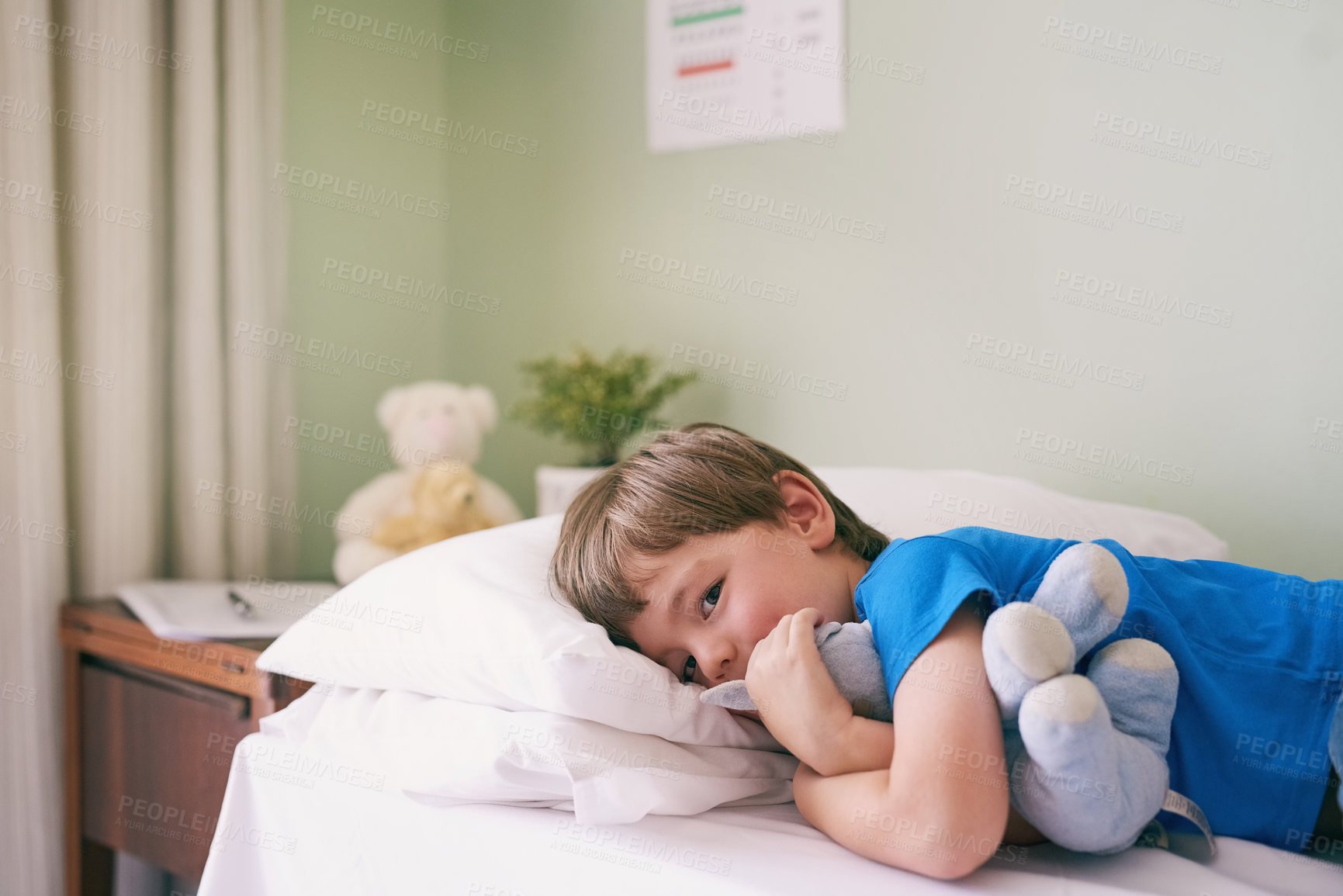Buy stock photo Shot of a little boy lying on a hospital bed while holding on tight to his stuffed animal