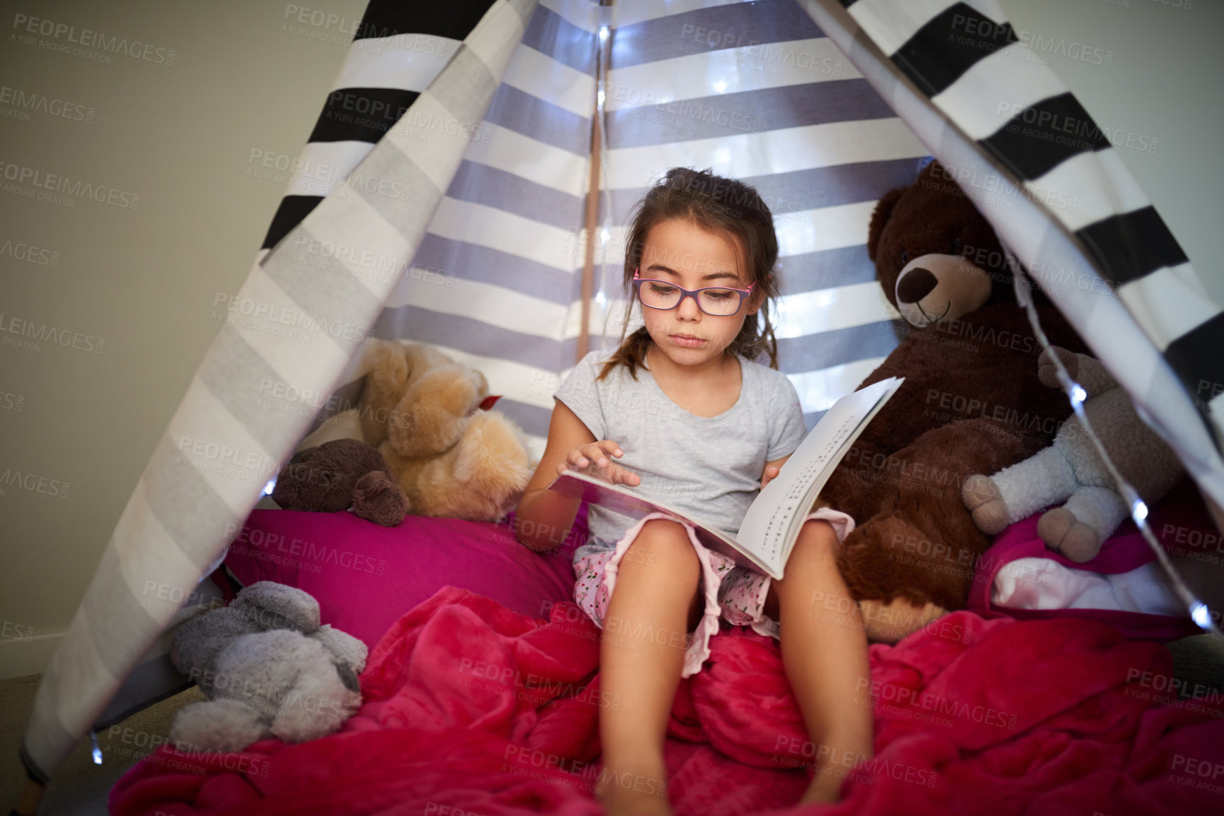 Buy stock photo Shot of a little girl reading a book with her teddybear in a tent at home