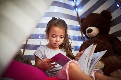 Buy stock photo Cropped shot of a little girl reading a book with her teddybear in a tent at home