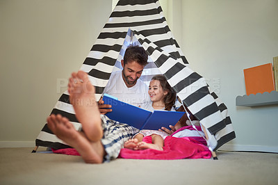 Buy stock photo Shot of a father reading a book with his little daughter in a tent at home