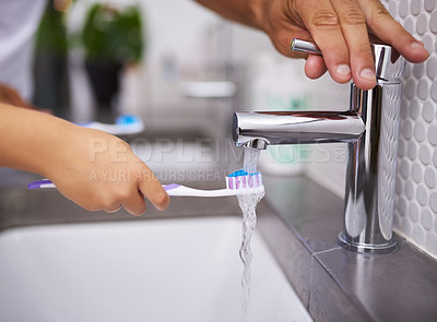Buy stock photo Shot of an unrecognizable man opening the tap while an unrecognizable child wets their toothbrush in the bathroom at home