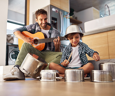 Buy stock photo Shot of a happy father accompanying his young son on the guitar while he drums on a set of cooking pots