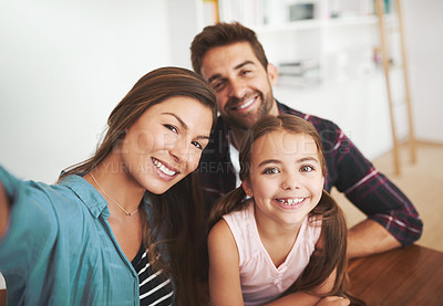 Buy stock photo Portrait of a happy married couple and their young daughter posing for a selfie together at home