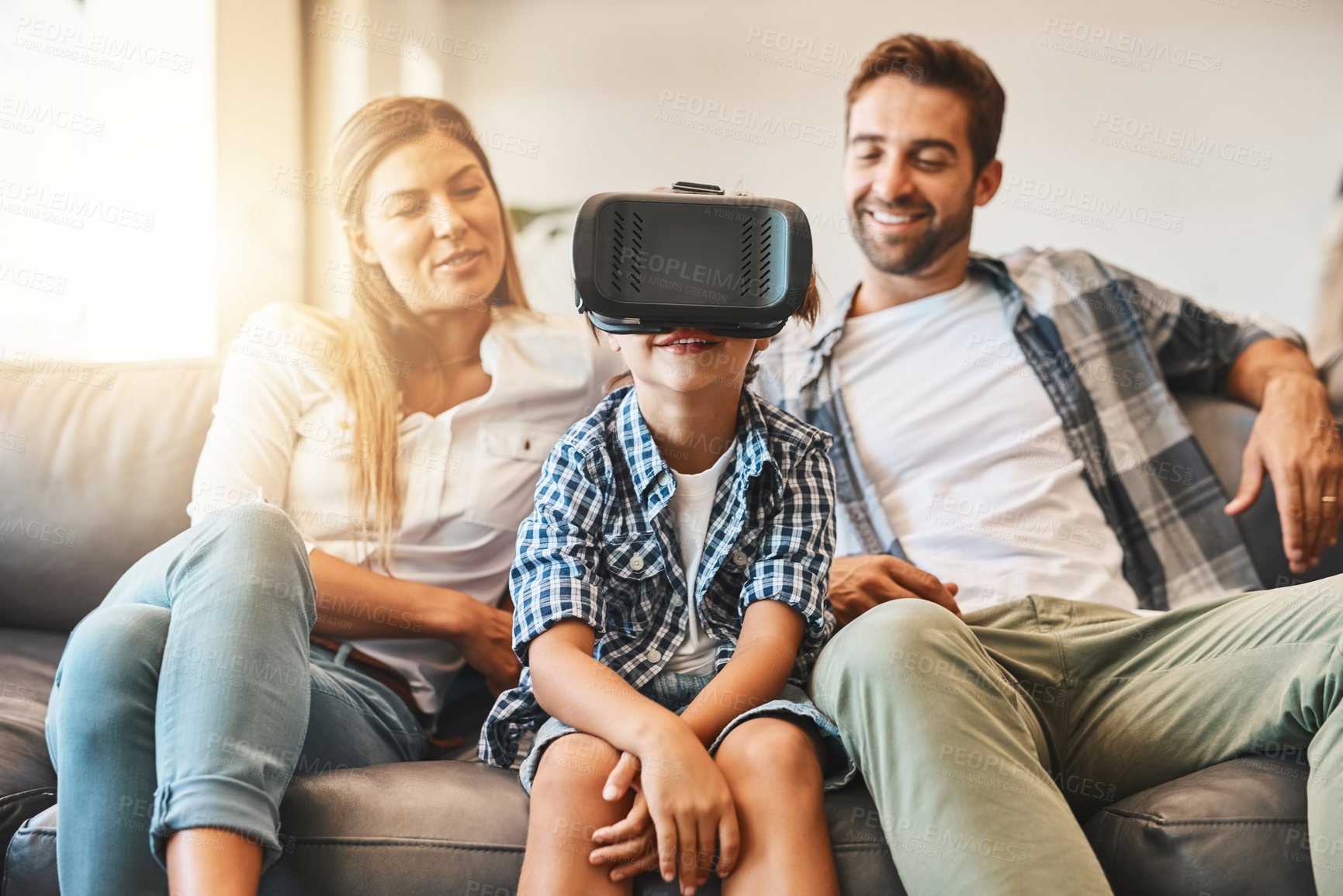 Buy stock photo Shot of a little boy using a virtual reality headset on the sofa at home with his parents