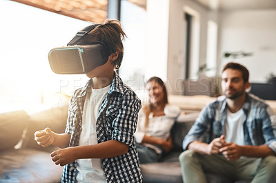 Buy stock photo Shot of a little boy using a virtual reality headset at home with his parents in the background