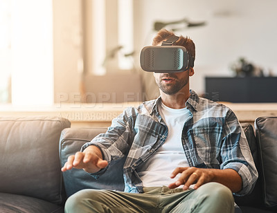 Buy stock photo Shot of a young man using a virtual reality headset on the sofa at home