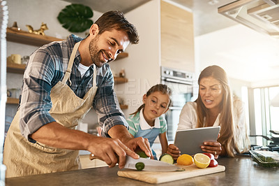 Buy stock photo Shot of two happy parents and their young daughter trying a new recipe in the kitchen together