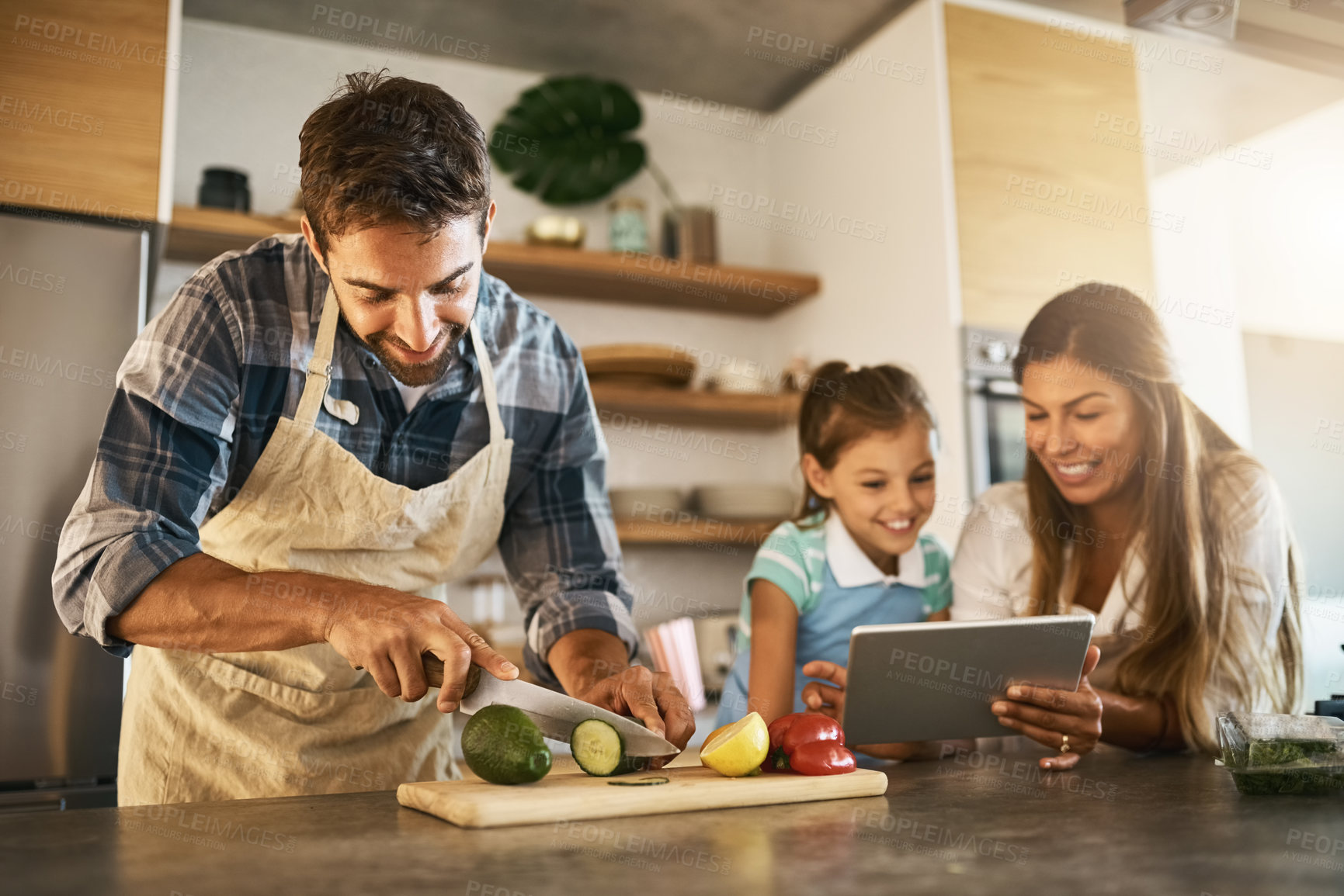 Buy stock photo Shot of two happy parents and their young daughter trying a new recipe in the kitchen together