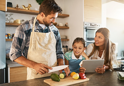 Buy stock photo Shot of two happy parents and their young daughter trying a new recipe in the kitchen together