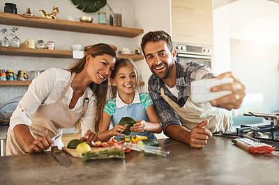 Buy stock photo Shot of a happy young family posing for a selfie while cooking together in their kitchen