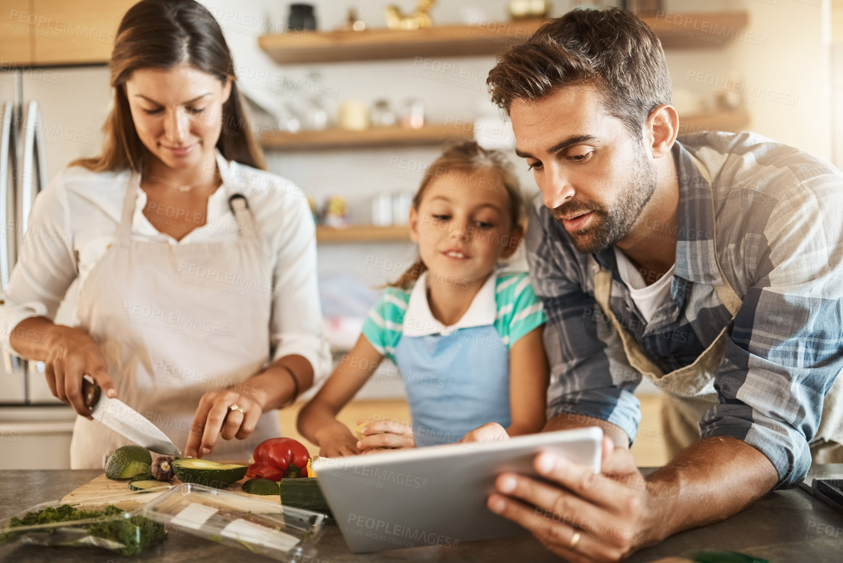 Buy stock photo Shot of two happy parents and their young daughter trying a new recipe in the kitchen together