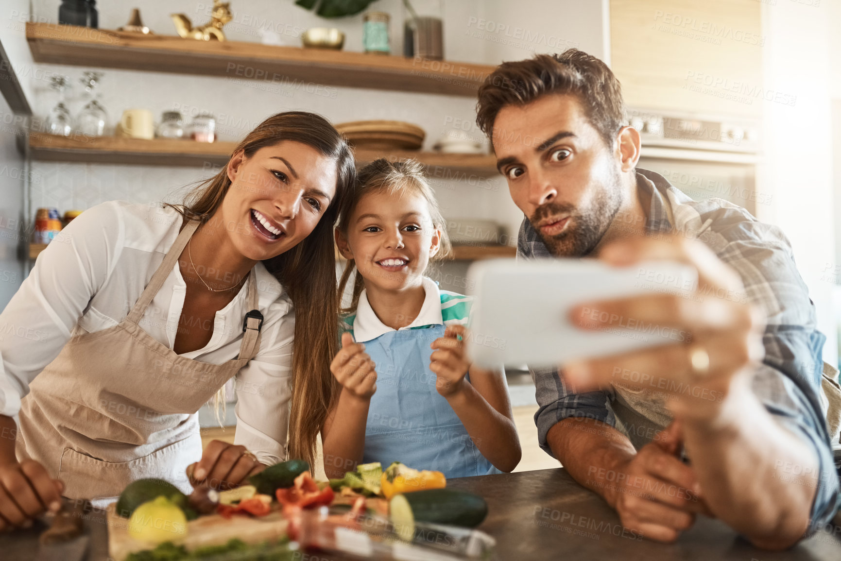 Buy stock photo Shot of a happy young family posing for a selfie while cooking together in their kitchen