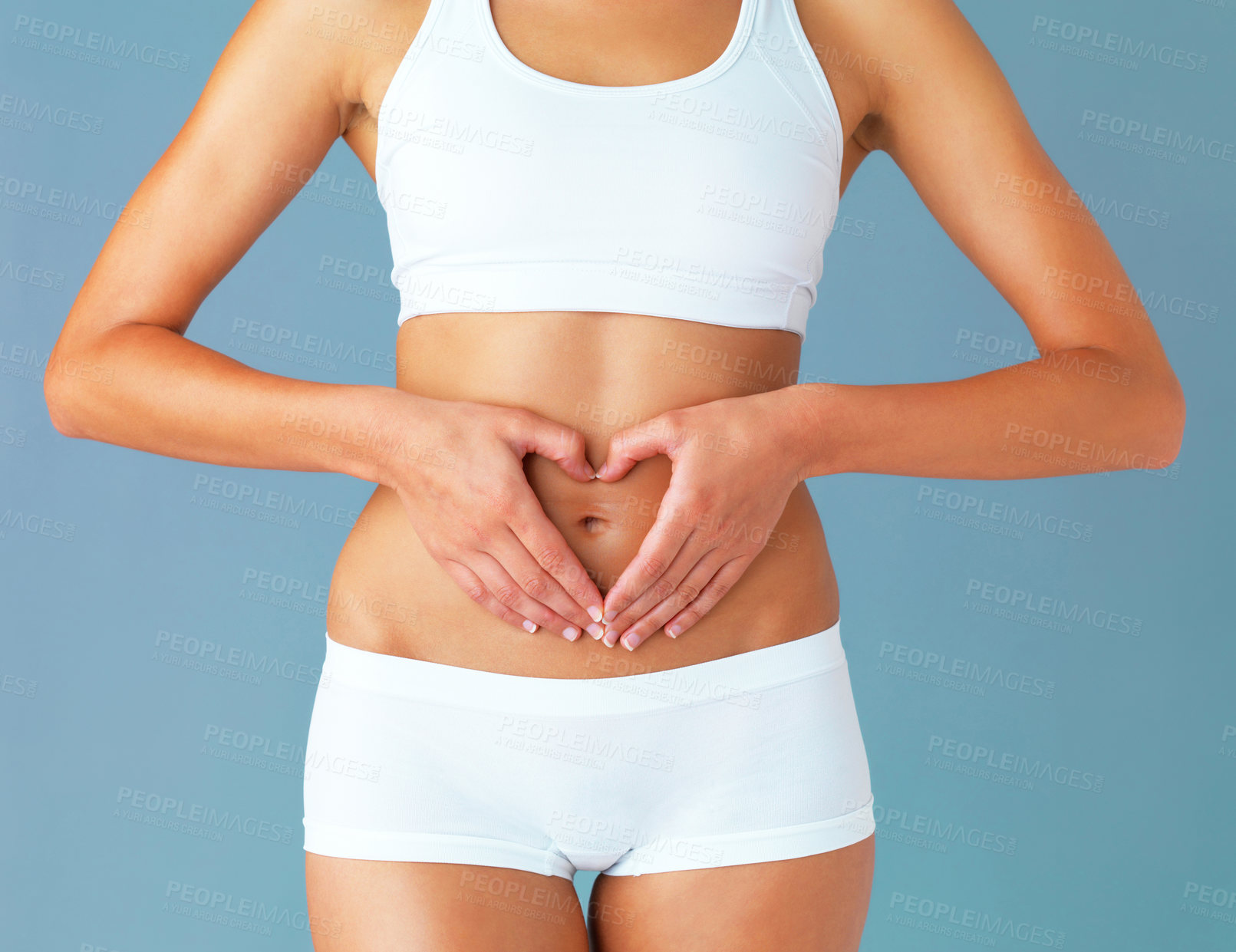 Buy stock photo Cropped studio shot of a fit young woman making a heart shaped gesture over her stomach against a blue background