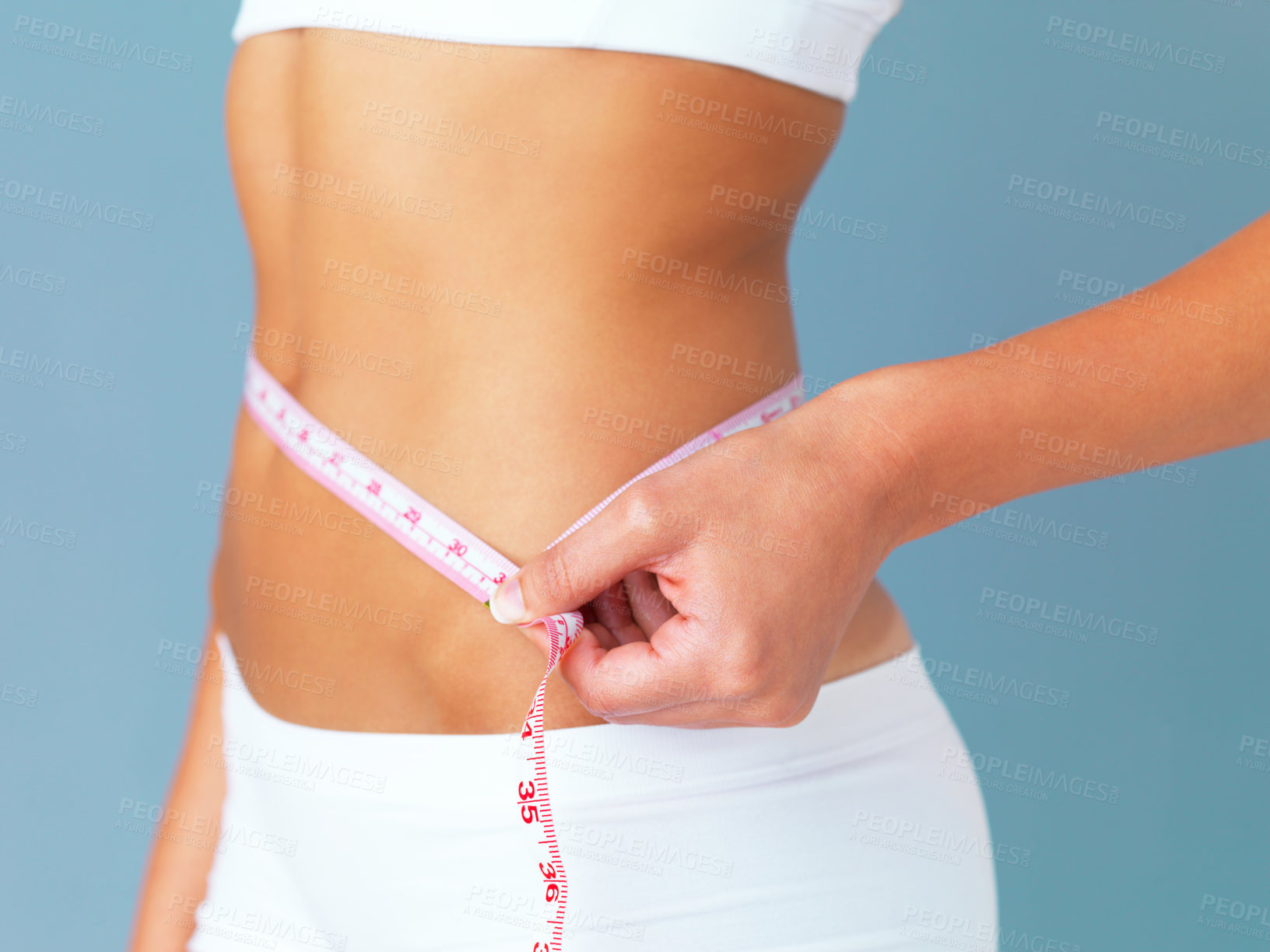 Buy stock photo Cropped studio shot of a fit young woman measuring her waist against a blue background