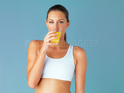 Buy stock photo Studio shot of a fit young woman drinking a glass of juice against a blue background