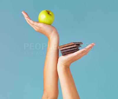 Buy stock photo Cropped studio shot of a woman holding up chocolate and an apple against a blue background