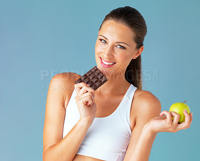 Buy stock photo Studio shot of a fit young woman holding an apple and a chocolate against a blue background