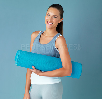 Buy stock photo Studio portrait of a healthy young woman holding an exercise mat against a blue background