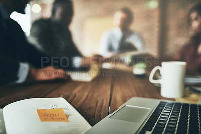 Buy stock photo Shot of a laptop and paperwork on a boardroom table with unidentifiable businesspeople meeting in the background