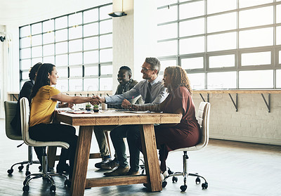 Buy stock photo Shot of two business colleagues shaking hands over the boardroom table during a meeting