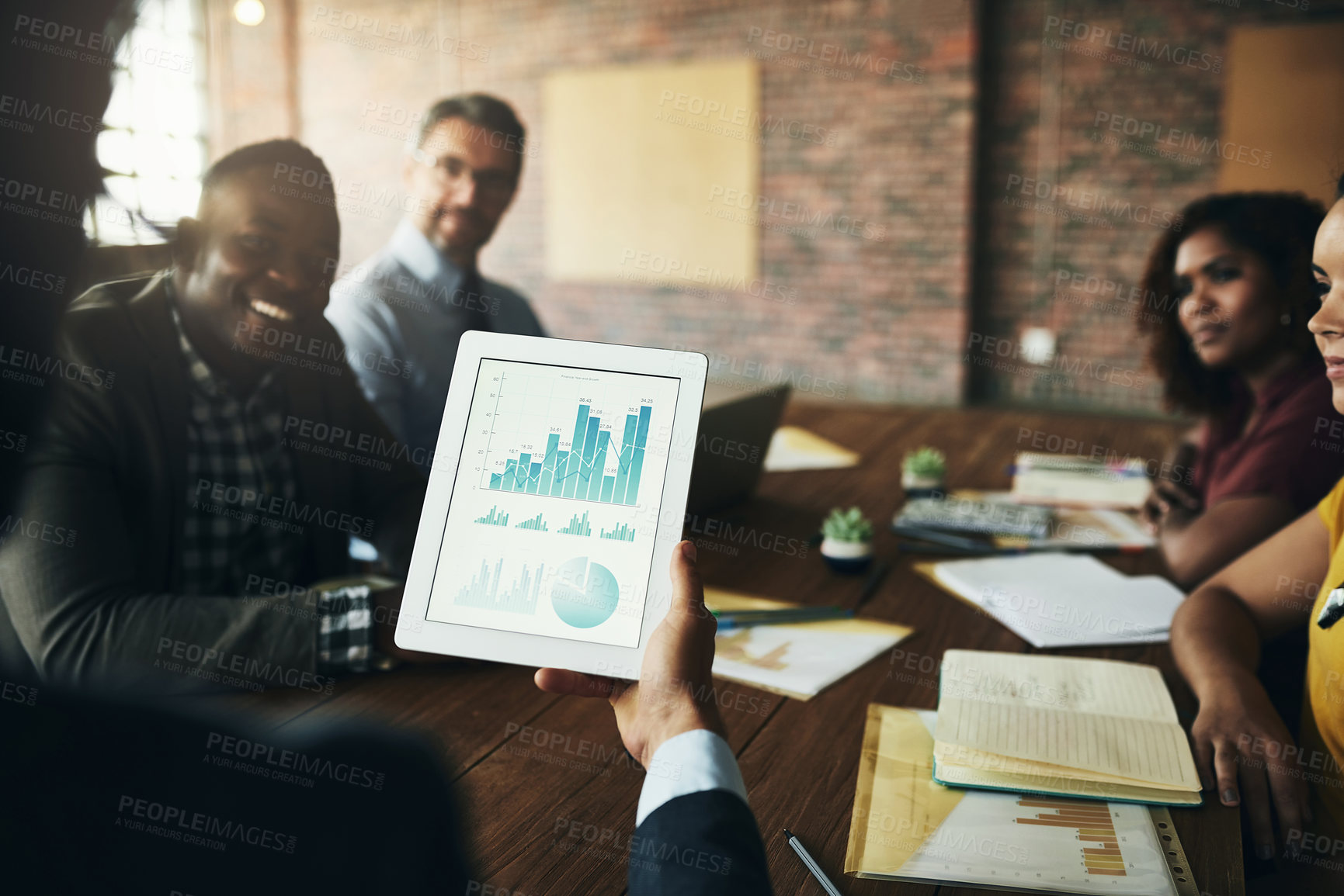 Buy stock photo Rearview shot of an unidentifiable businessman looking at graphs on his tablet during a meeting with his colleagues