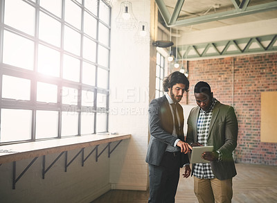 Buy stock photo Shot of two well-dressed businessmen brainstorming together over a tablet in their office