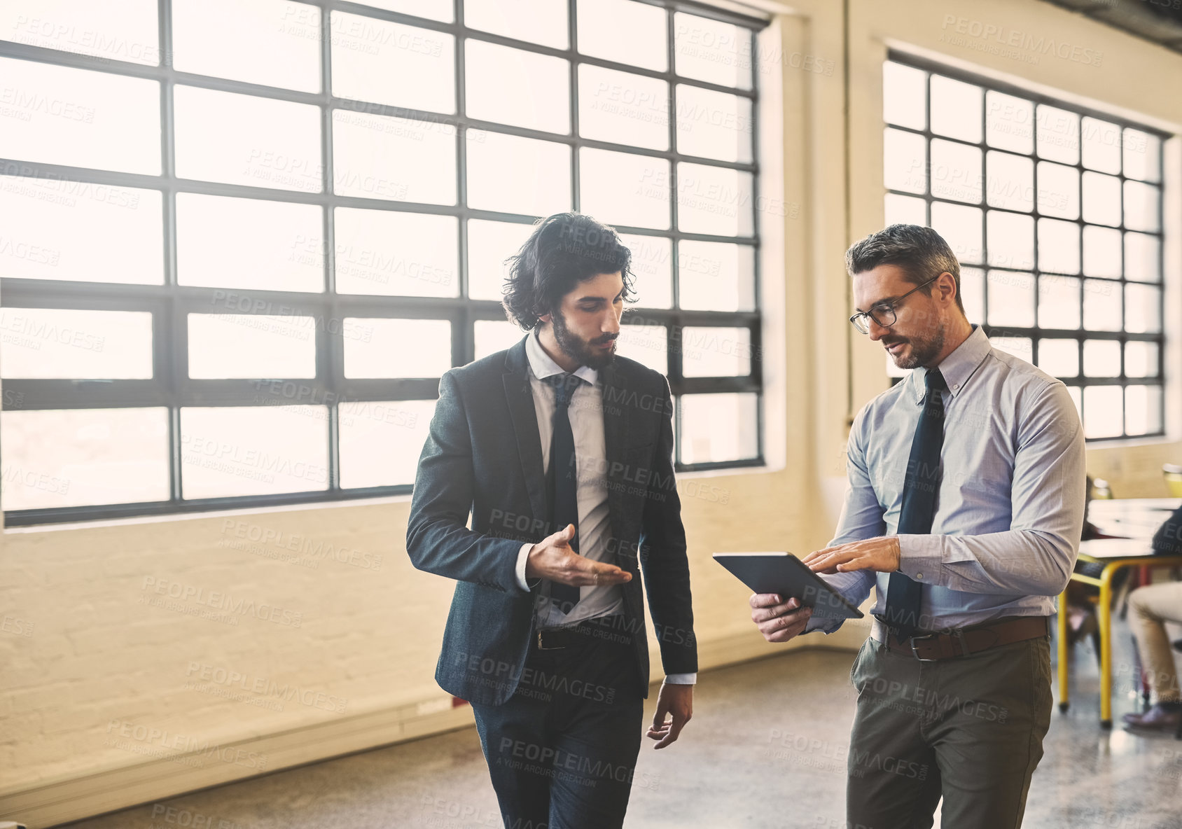 Buy stock photo Shot of two well-dressed businessmen brainstorming together over a tablet in their office