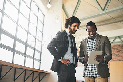 Buy stock photo Shot of two well-dressed businessmen brainstorming together over a tablet in their office