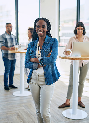 Buy stock photo Portrait of a confident young woman standing in a modern office with her colleagues in the background