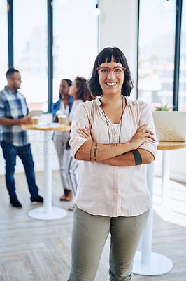 Buy stock photo Portrait of a confident young woman standing in a modern office with her colleagues in the background