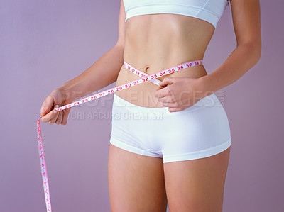 Buy stock photo Studio shot of a healthy woman measuring her waistline with a tape measure against a purple background