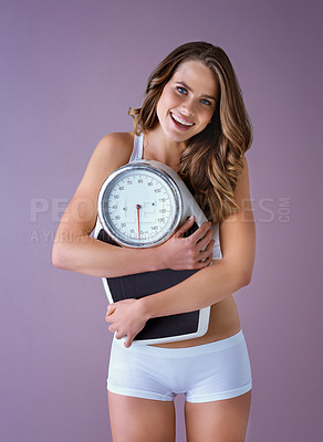 Buy stock photo Studio shot of a healthy young woman smiling and holding a scale against a purple background