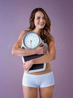 Buy stock photo Studio shot of a healthy young woman smiling and  holding a scale against a purple background