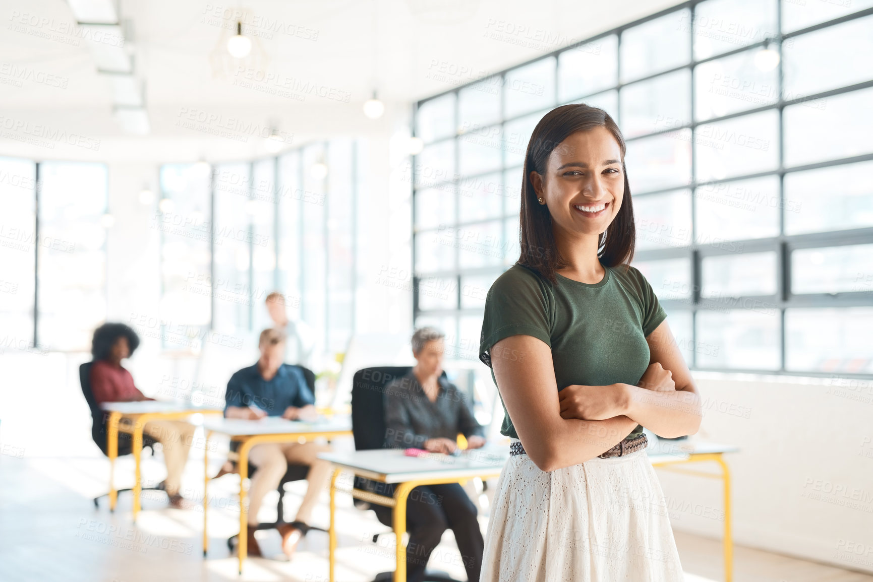 Buy stock photo Portrait of a happy designer posing in the office while her colleagues work in the background