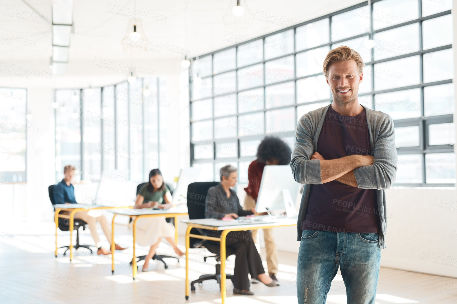 Buy stock photo Portrait of a happy designer posing in the office while his colleagues work in the background