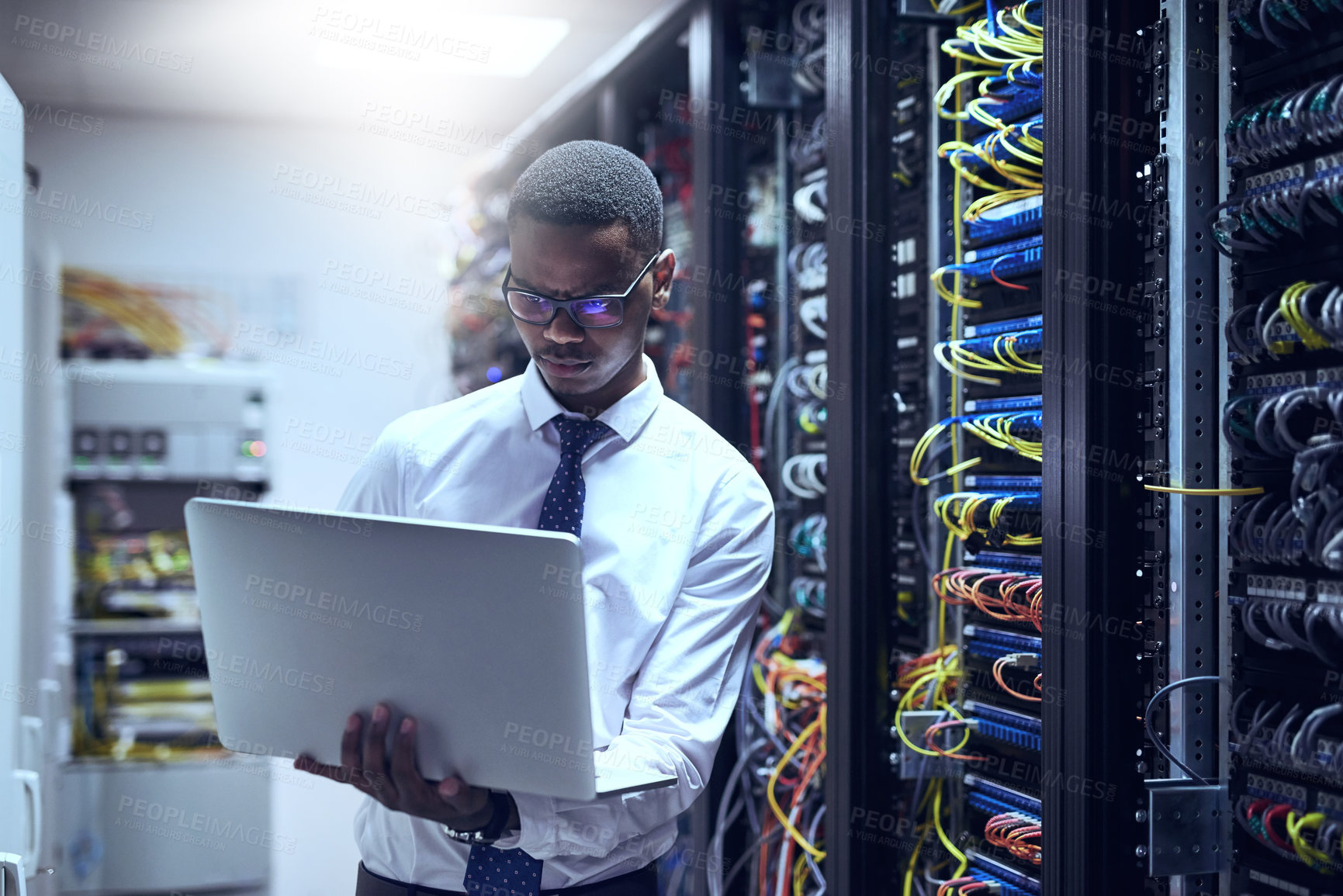 Buy stock photo Cropped shot of a IT technician working on his laptop while standing inside of a server room