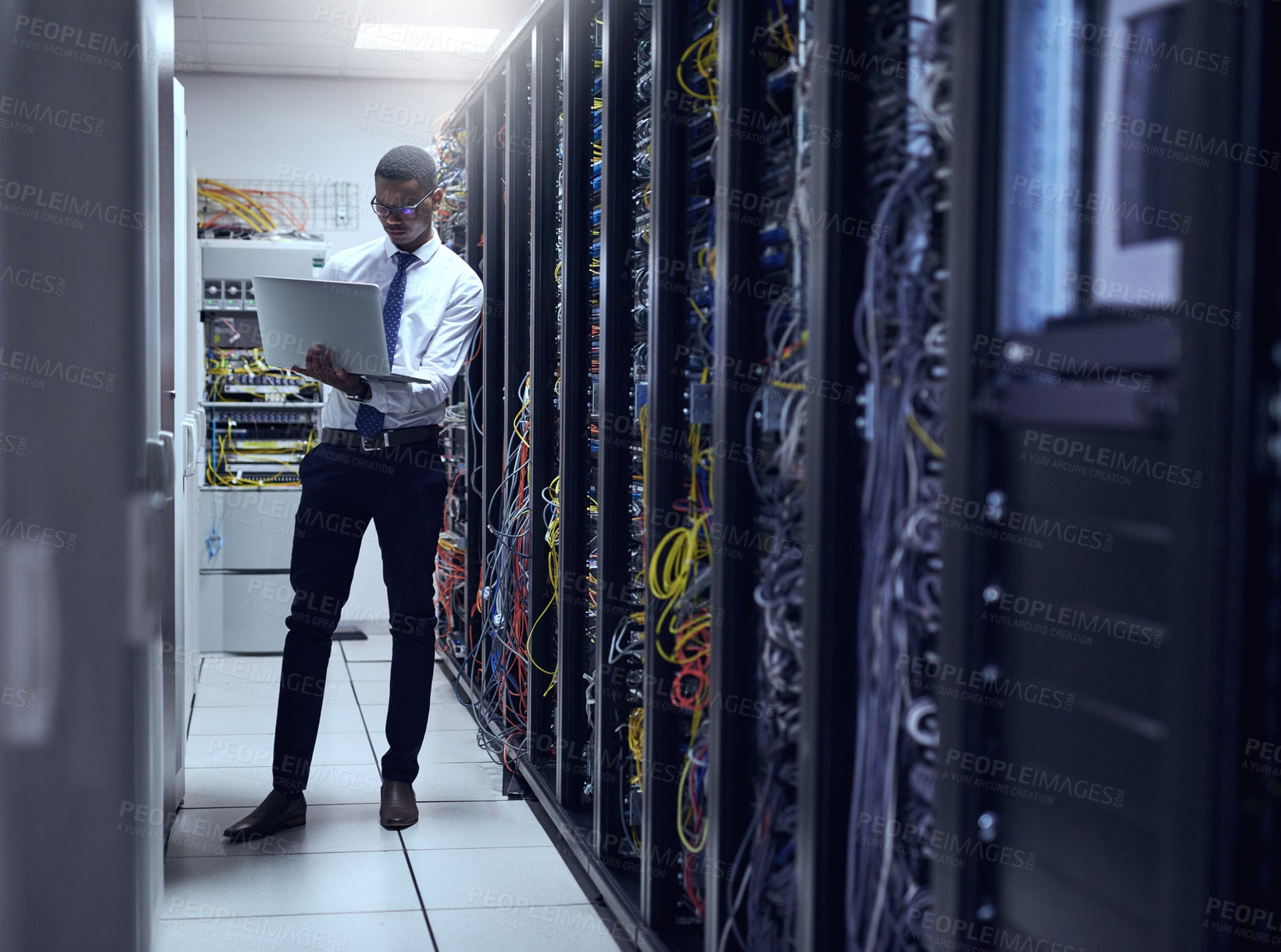 Buy stock photo Cropped shot of a IT technician working on his laptop while standing inside of a server room