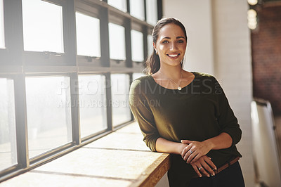 Buy stock photo Portrait of a confident young businesswoman standing at a window in an office