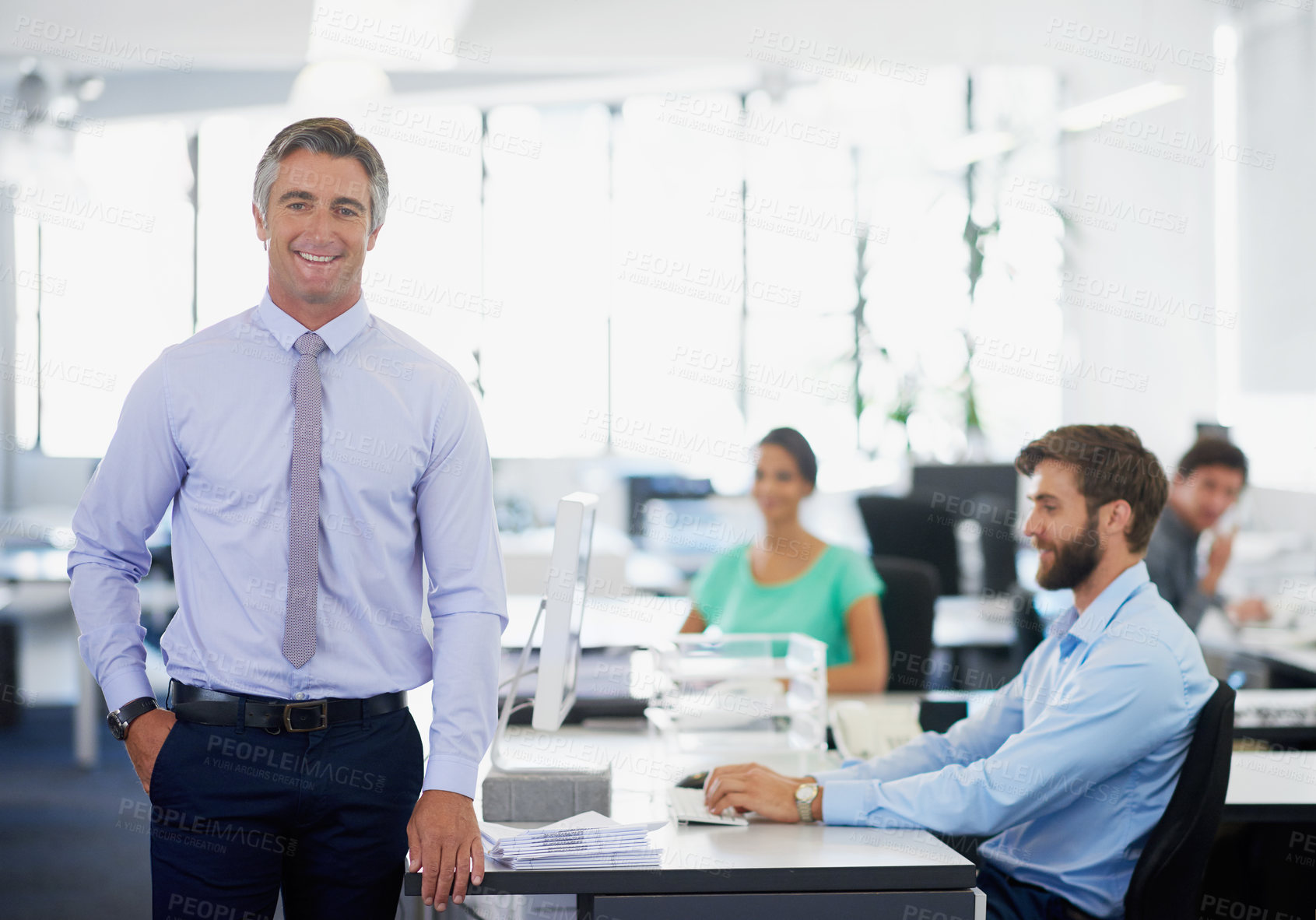 Buy stock photo Portrait of a handsome mature businessman standing in an office with his employees in the background