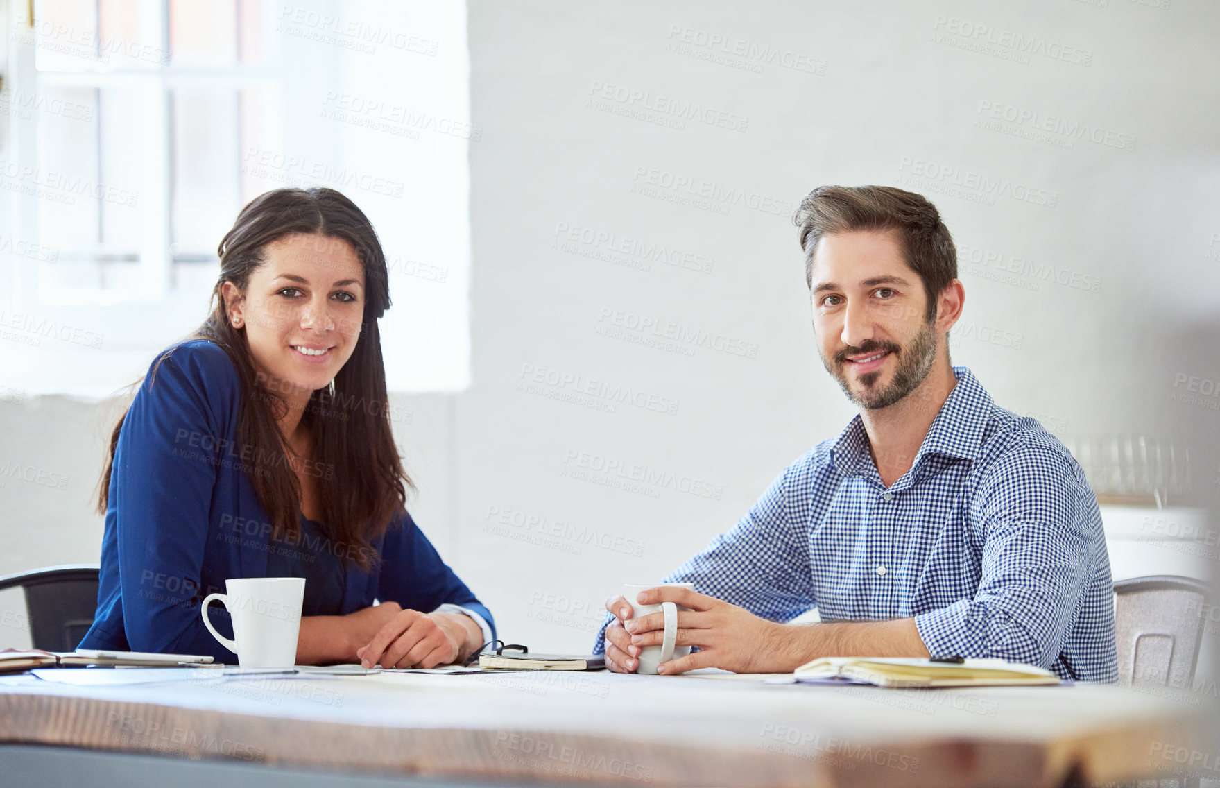 Buy stock photo Cropped portrait of two young businesspeople sitting at a table in the office