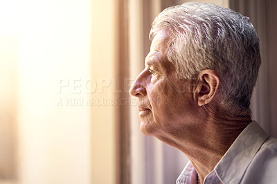 Buy stock photo Shot of a thoughtful senior man looking out of the window at home
