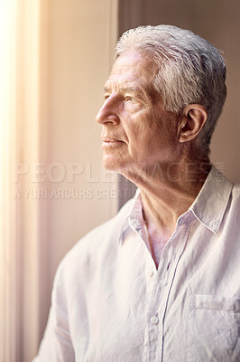 Buy stock photo Shot of a thoughtful senior man looking out of the window at home