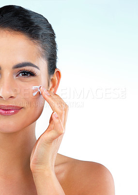 Buy stock photo Studio shot of a beautiful young woman applying ointment onto her face  against a blue background