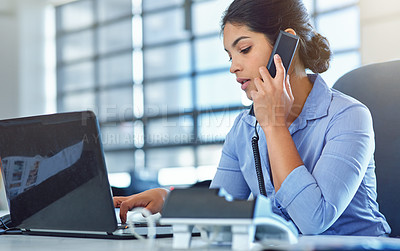 Buy stock photo Shot of a young businesswoman answering a phone while using her laptop at her desk