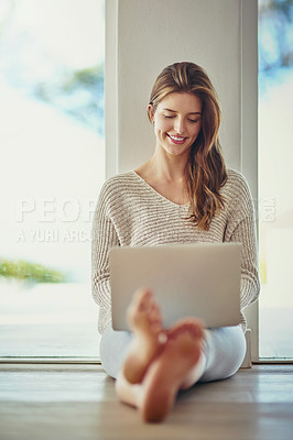 Buy stock photo Shot of a happy young woman using her laptop while sitting on the floor at home