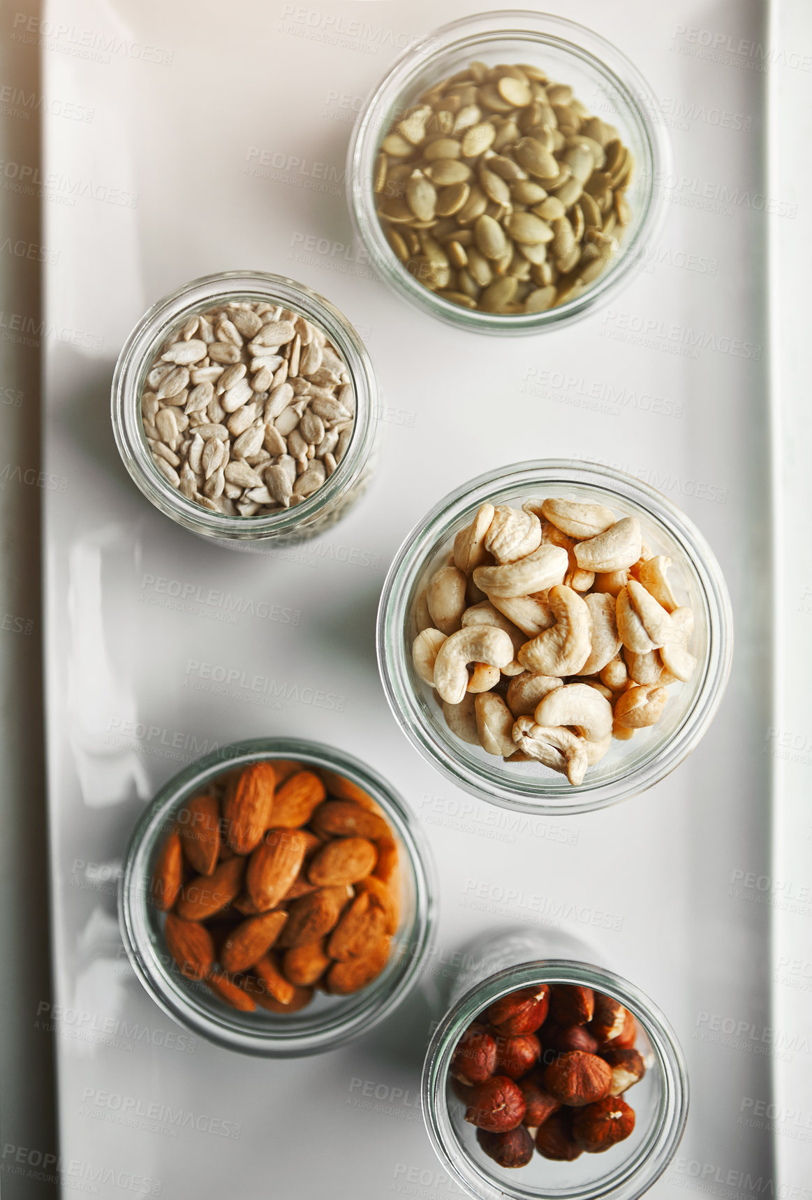 Buy stock photo Bowls, nuts and seeds on plate, above and hazelnut for nutrition, health and table with diet for wellness. Cashew, almond and pumpkin in glass container for meal prep with food in morning at house