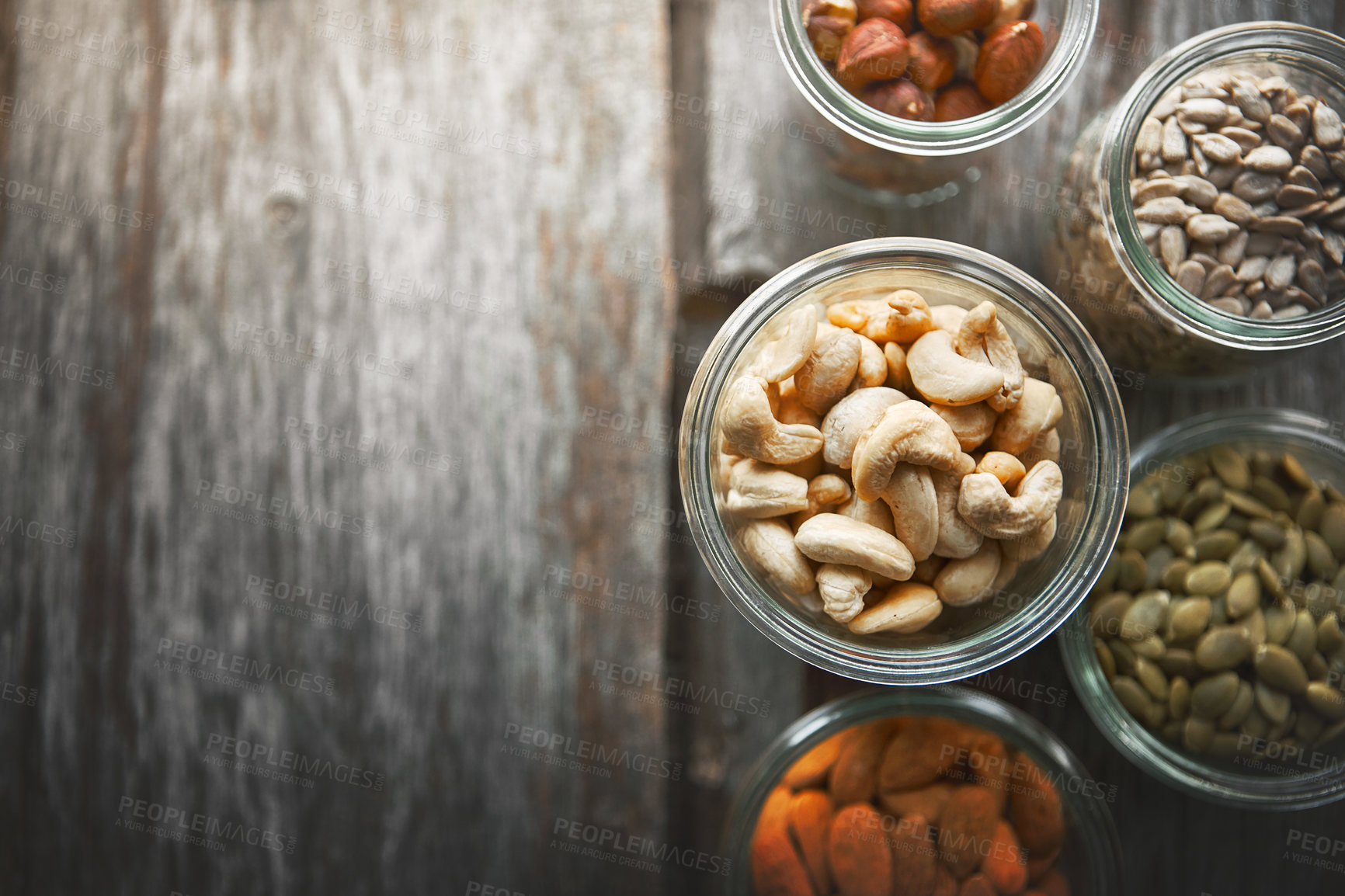 Buy stock photo Bowls, cashew and nuts on table, above and mock up space for nutrition, health and promotion for wellness. Almond, hazelnut and pumpkin seeds in glass container for meal prep with food at apartment