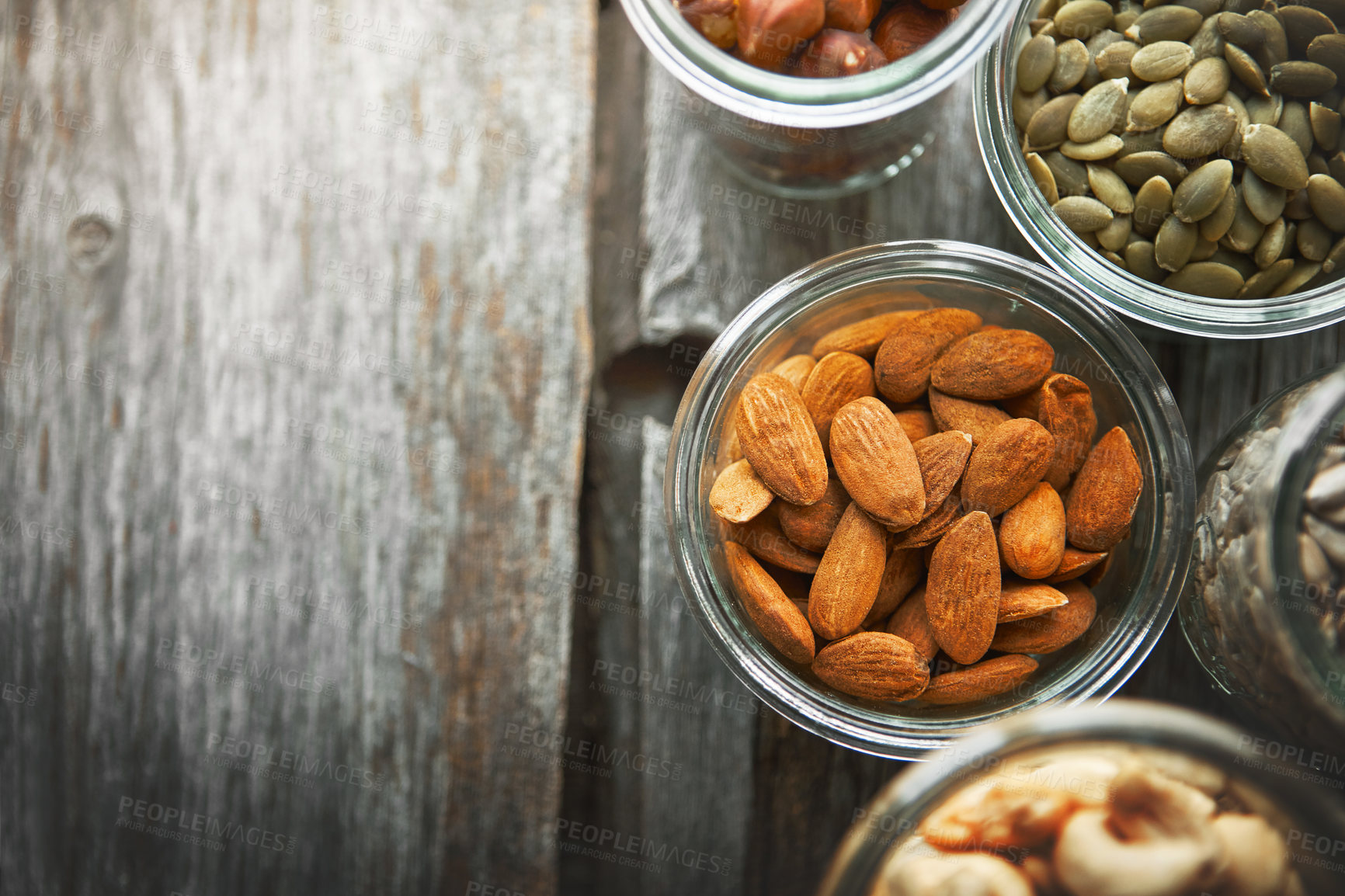 Buy stock photo Bowls, almond and nuts on table, above and mock up space for nutrition, health and promotion for wellness. Cashew, hazelnut and pumpkin seeds in glass container for meal prep with food at apartment