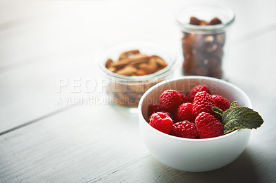 Buy stock photo Shot of fresh raspberries in a bowl with nuts blurred in the background