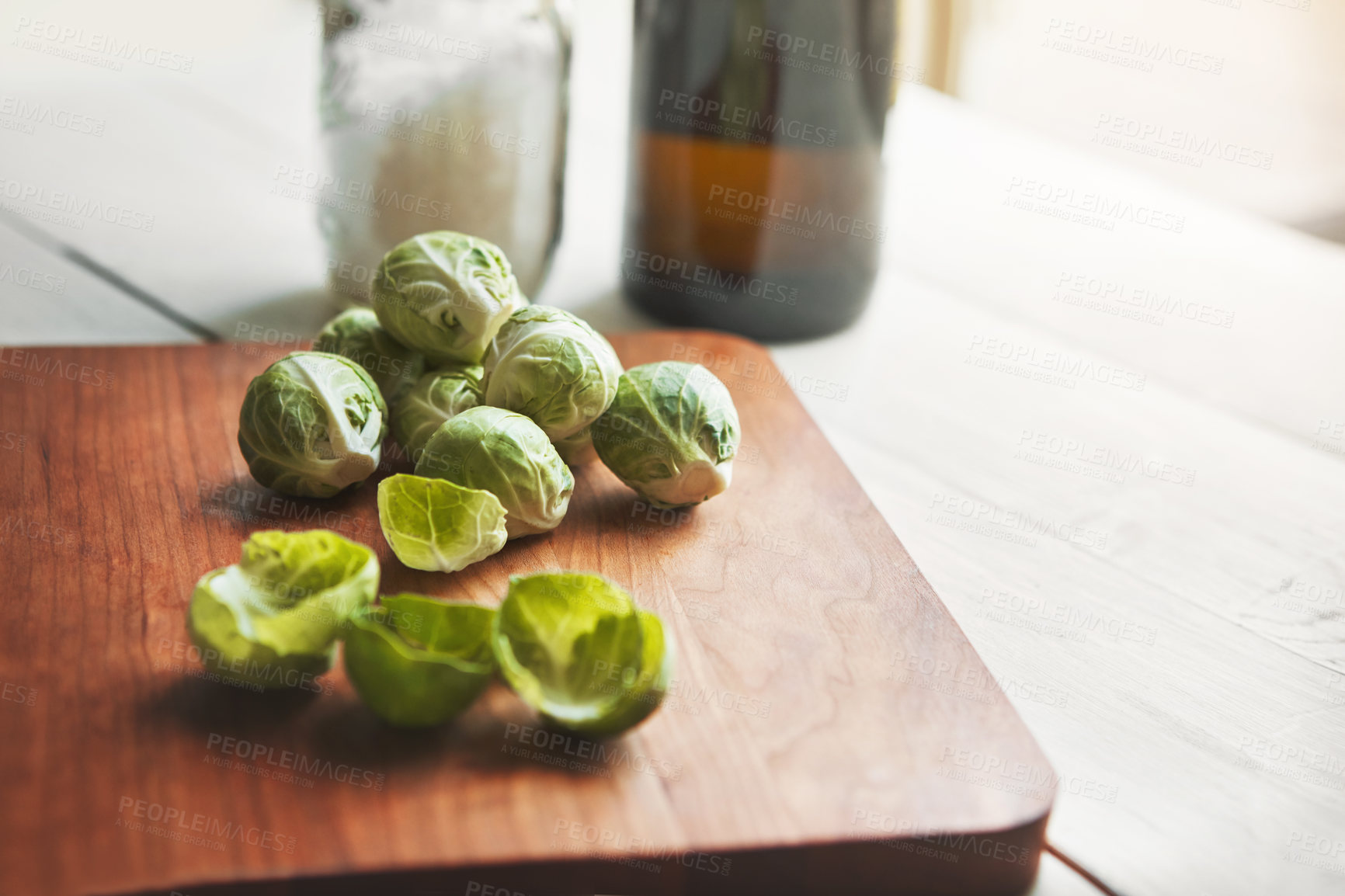 Buy stock photo Brussels sprouts, wooden board and food in home for health, lunch and nutrition for wellness. Vegetables, cooking and chopping block on table, leaves and meal prep for dinner on vegan diet in kitchen